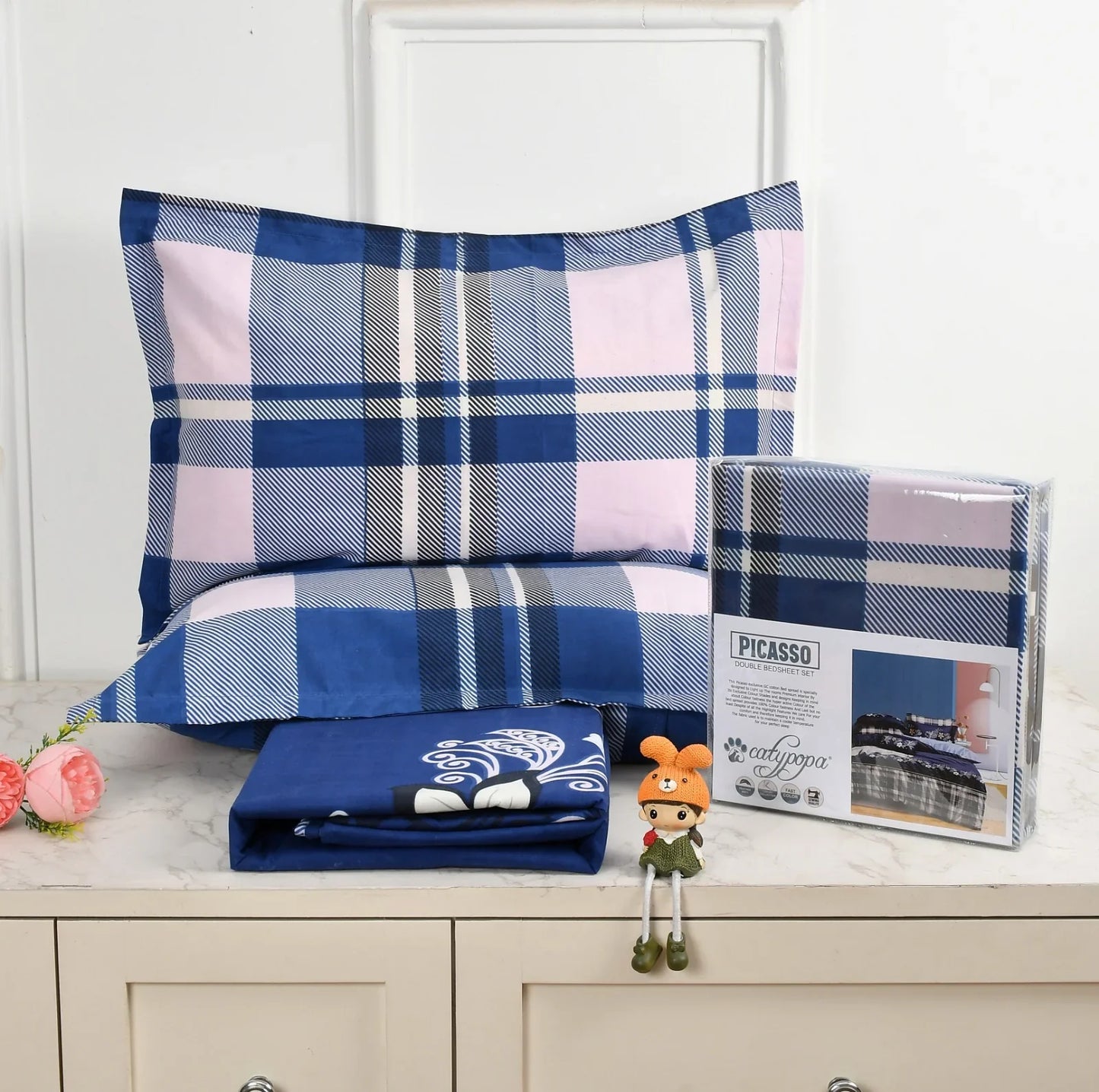 Navy blue and pink plaid checkered bedsheet set with white stripes - Picasso collection 3PC cotton bedding set with tartan design by Towelleo.com displayed on white dresser with decorative flowers and packaging