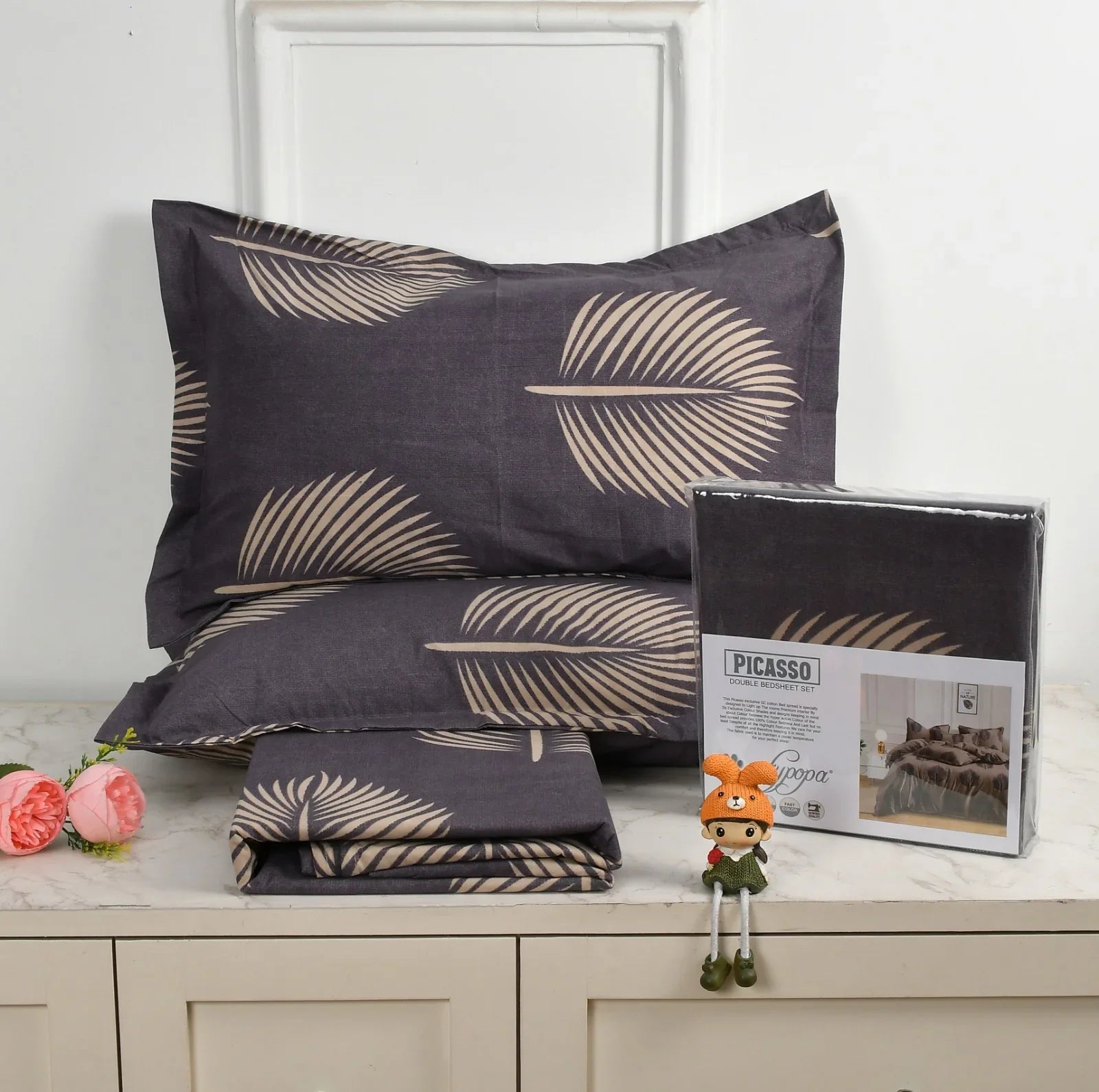 Charcoal grey bedsheet set with gold palm leaf pattern - Picasso collection 3PC cotton bedding set with tropical design by Towelleo.com displayed on white dresser with decorative flowers and packaging
