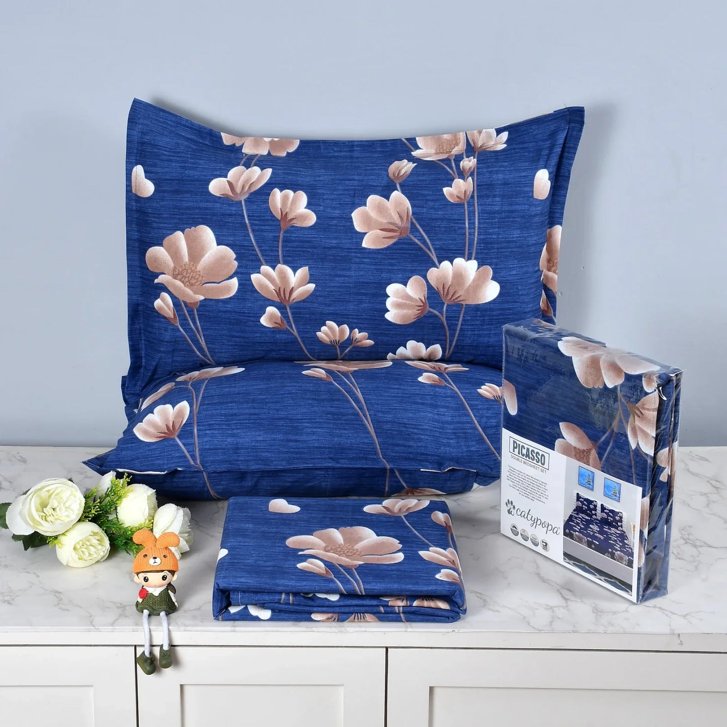 Royal blue bedsheet set with pink magnolia flower pattern on textured fabric - Picasso collection 3PC cotton bedding set with elegant floral design by Towelleo.com displayed on white dresser with decorative flowers and packaging
