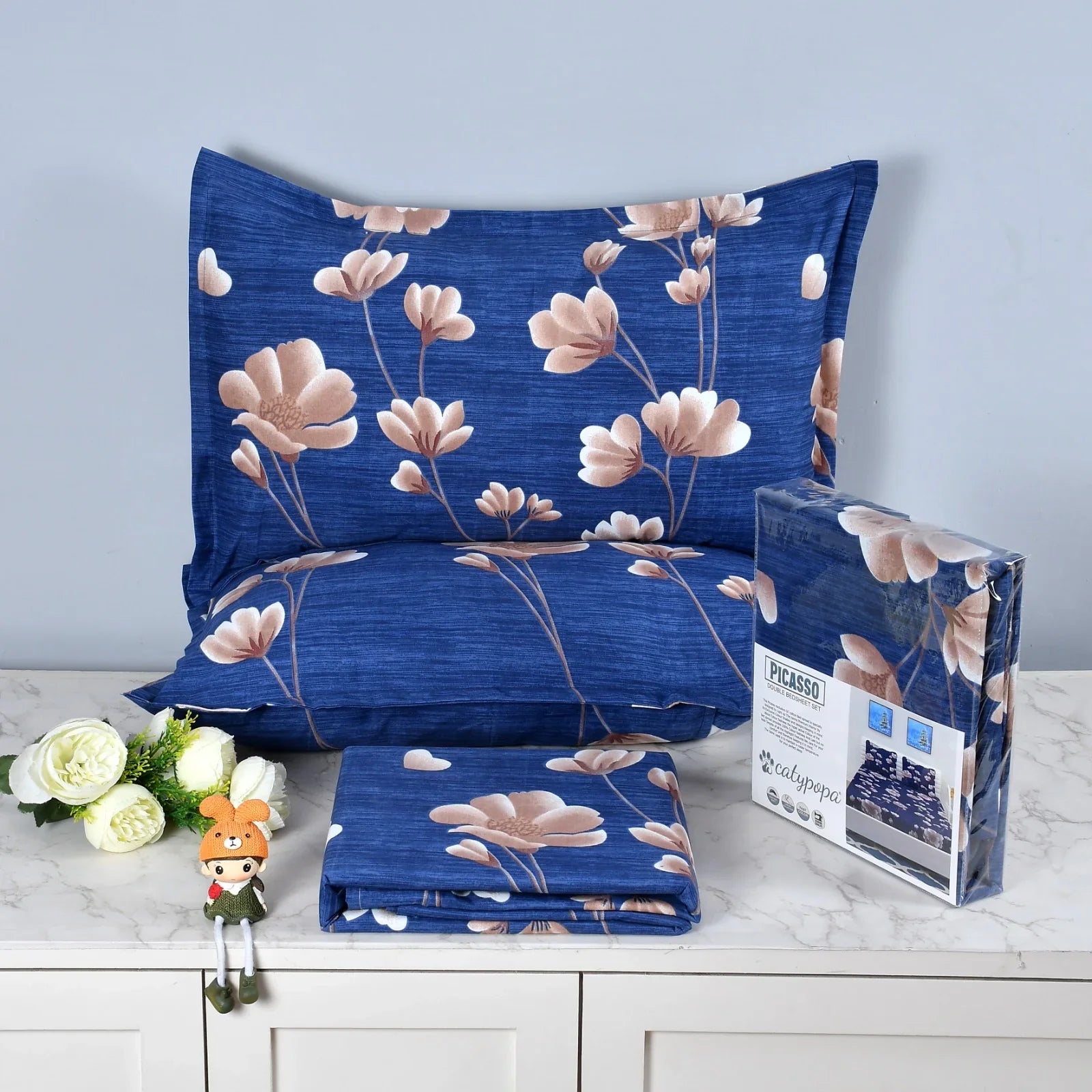 Royal blue bedsheet set with pink magnolia flower pattern on textured fabric - Picasso collection 3PC cotton bedding set with elegant floral design by Towelleo.com displayed on white dresser with decorative flowers and packaging
