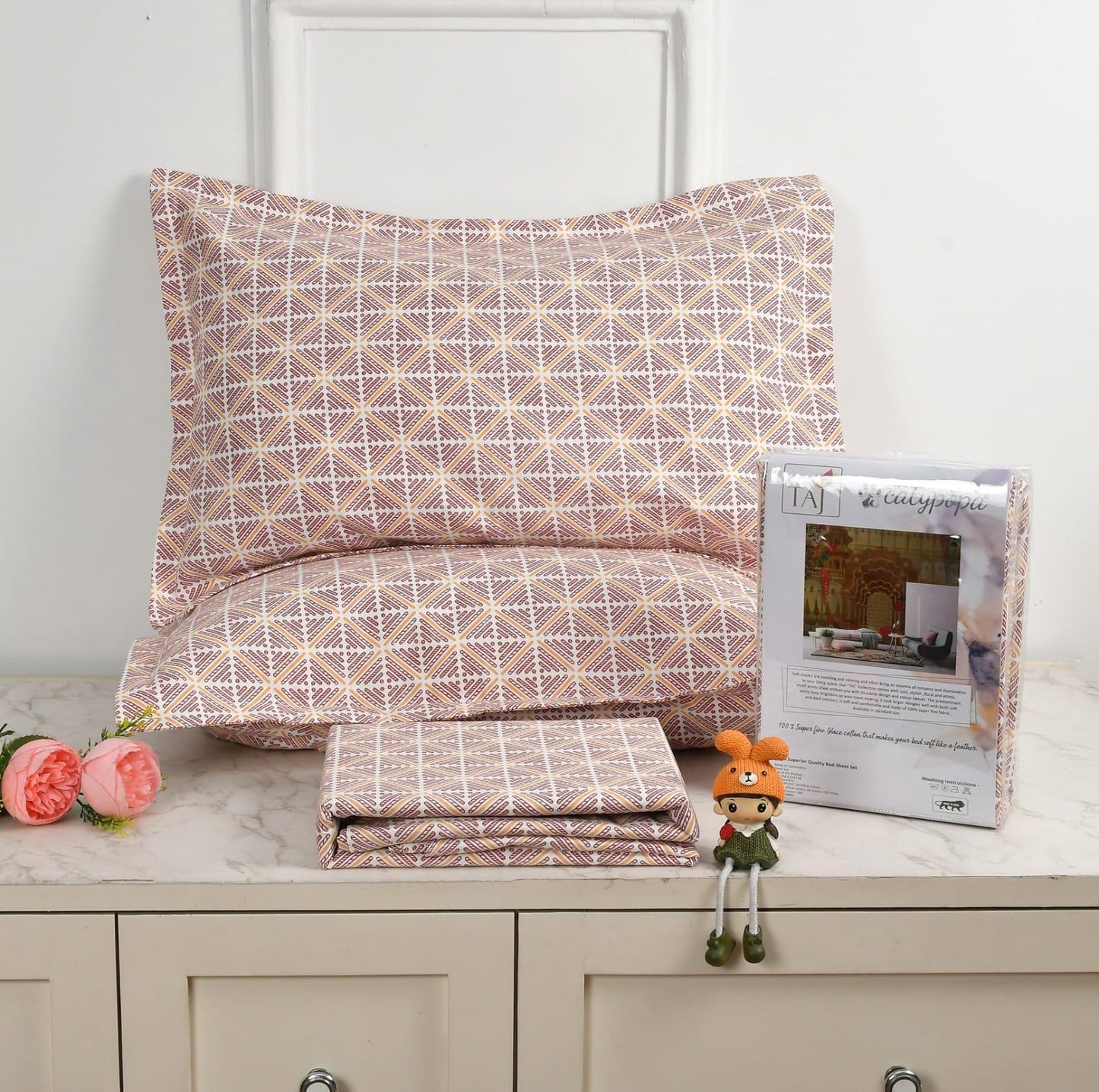 Patterned bedding set with a pillow and folded sheet on a surface, accompanied by a toy and product packaging towelleo.com